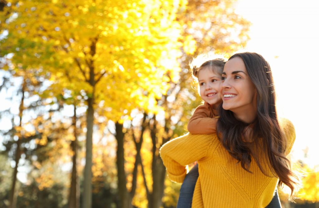 Happy woman with little daughter in sunny park. Autumn walk